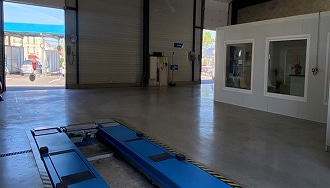 Contrôle Technique Automobile : Fosse et Espace Client Intérieur d'un centre de contrôle technique automobile moderne, avec un pont élévateur encastré bleu au premier plan et des baies vitrées menant à une zone d'attente.